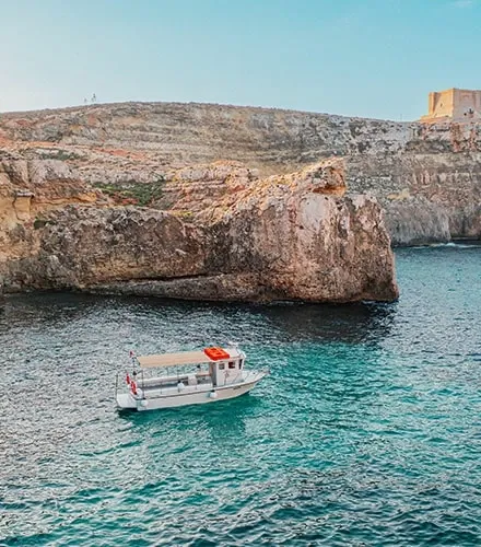 Comino Land boat beside the rocky Comino coast